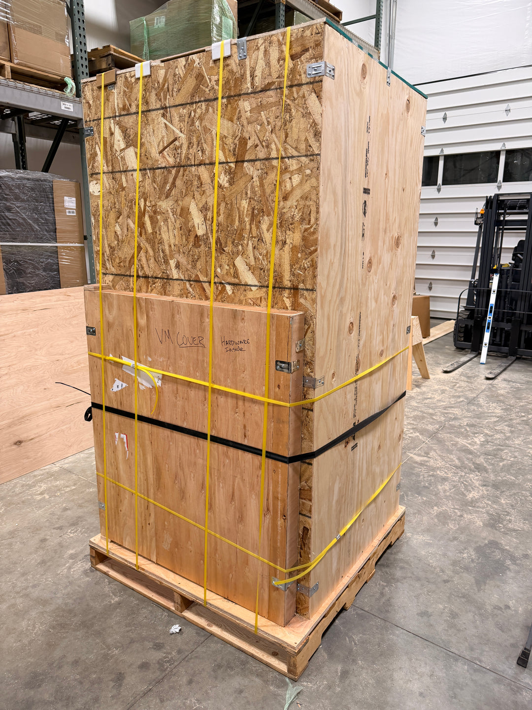 Stack of wooden pallets tied together with yellow straps in a warehouse setting.