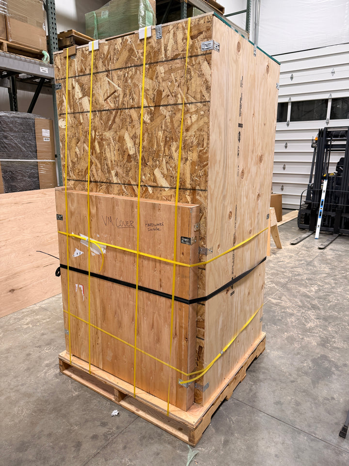 Stack of wooden pallets tied together with yellow straps in a warehouse setting.