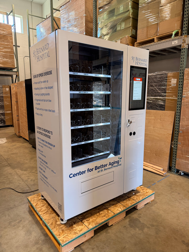Custom-branded Naloxone vending machine for St. Bernard Hospital. Features personalized graphics with opioid overdose signs, 5-step response guide, and integrated video screen for community harm reduction programs.